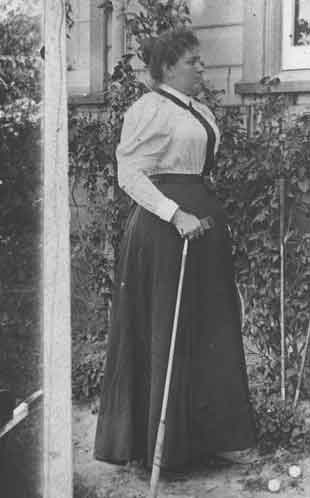 P825 Mrs JJ McCue (wife of Mr James J McCue Poultry and Bee Manager Hawkesbury Agricultural College 1897-1901) - standing outside a residence holding a golf iron with two golf balls at her feet Hawkesbury Agricultural College (HAC) c.1897