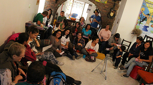 A large group sits in a circle on chairs and the floor, in discussion.