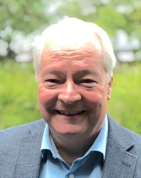 photo of Kurt, smiling at the camera, fair skin, white hair, blue shirt and jacket, grass and trees in background
