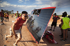 Student running past a solar car being fixed.