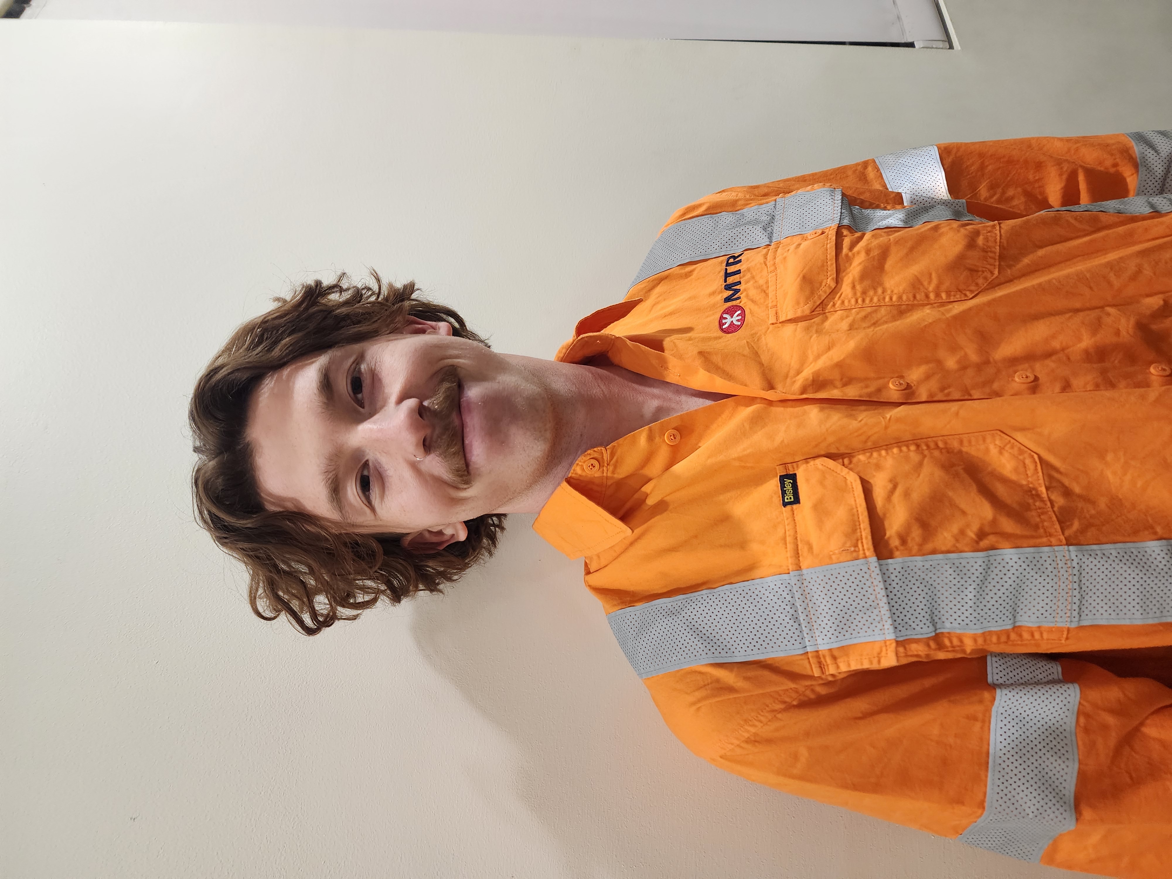 photo of person looking at camera, short brown wavy hair, wearing orange high visibility shirt