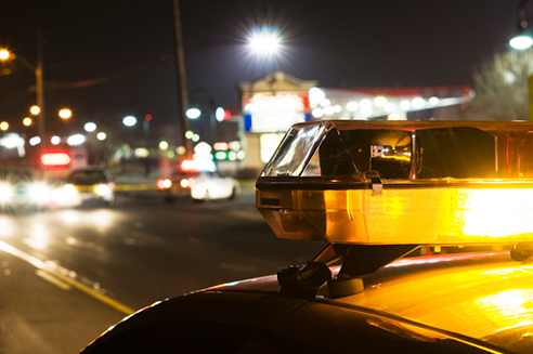 The flashing light of a police car as it drives down the street at night, with other cars and buildings out of focus in the distance.