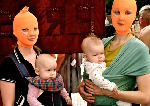 Two young women holding children with orange balaklavas