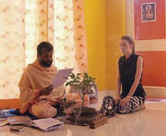 Steph Baker kneeling on the floor with an indian man holding a piece of paper