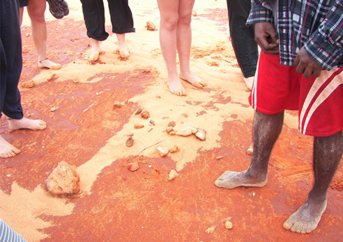 The feet of a group of people standing on the red rock.