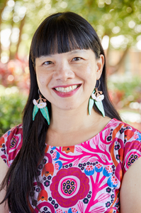 Quah Ee Ling smiles at the camera. She is wearing a bright pink and blue apttern shirt, and has long black hair. She wears white and green earrings.