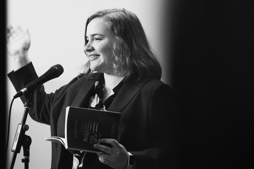 black and white photo of a smiling woman holding a book and speaking