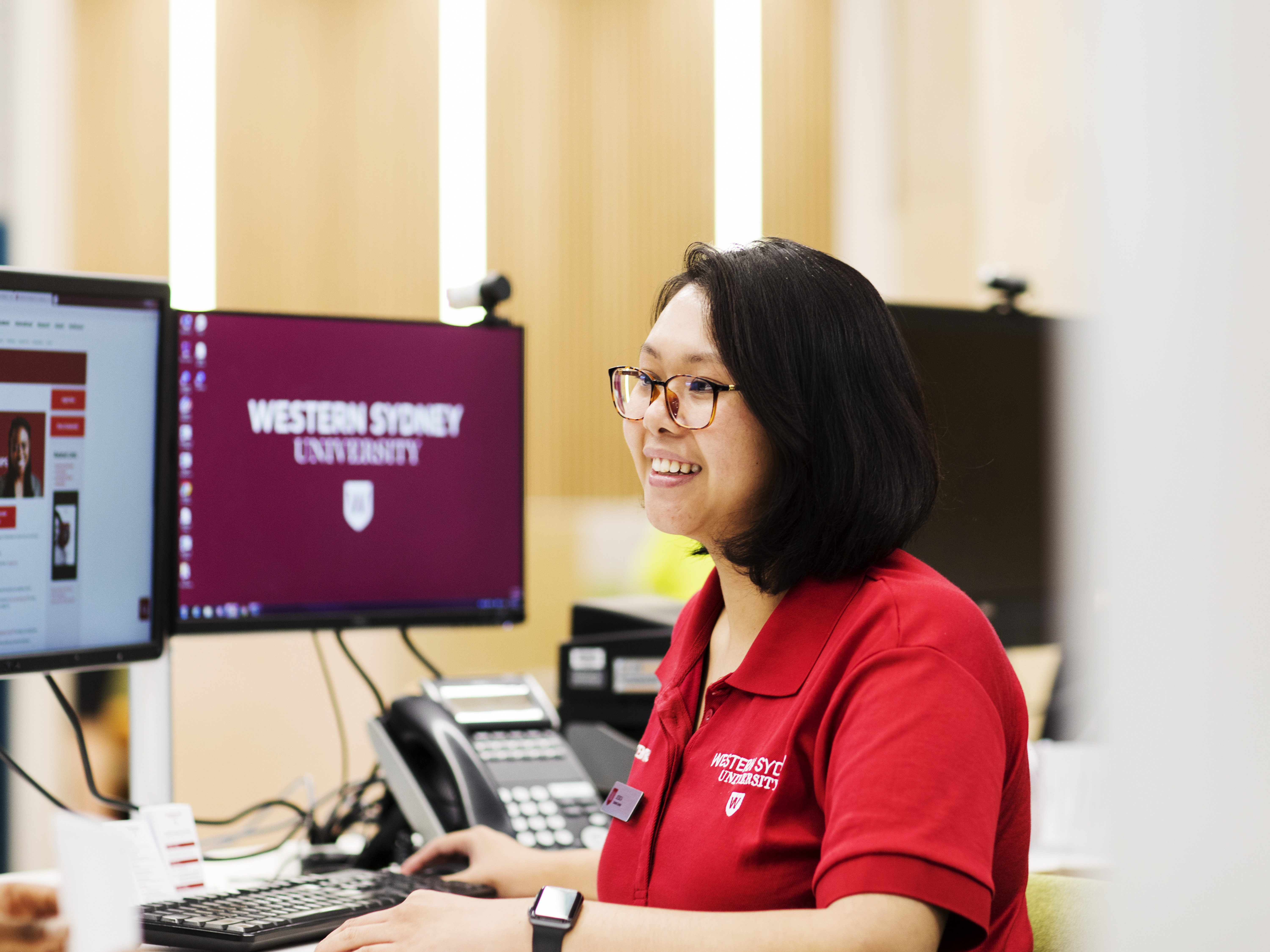 photo of person with fair skin and dark hair , wearing spectacles and a red shirt with a Western logo visible, sitting in front of a computer
