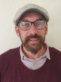 portrait photograph of a man with a beard, wearing glasses and a hat