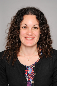 A woman with curly brown hair smiles at the camera.