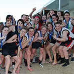 With medals around their necks, members of a women's AFL team smile for the camera, making 'Number 1' signs with their hands.
