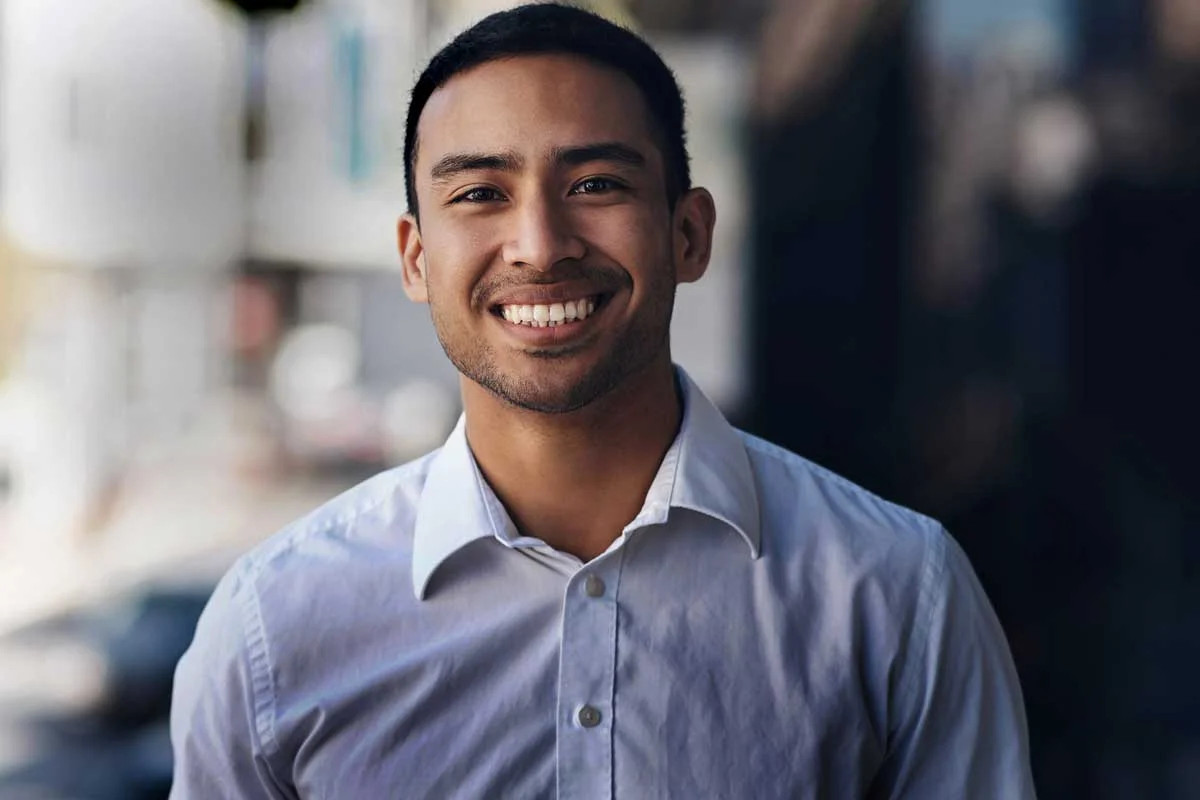 Man in blue collard shirt standing outside smiling at the camera