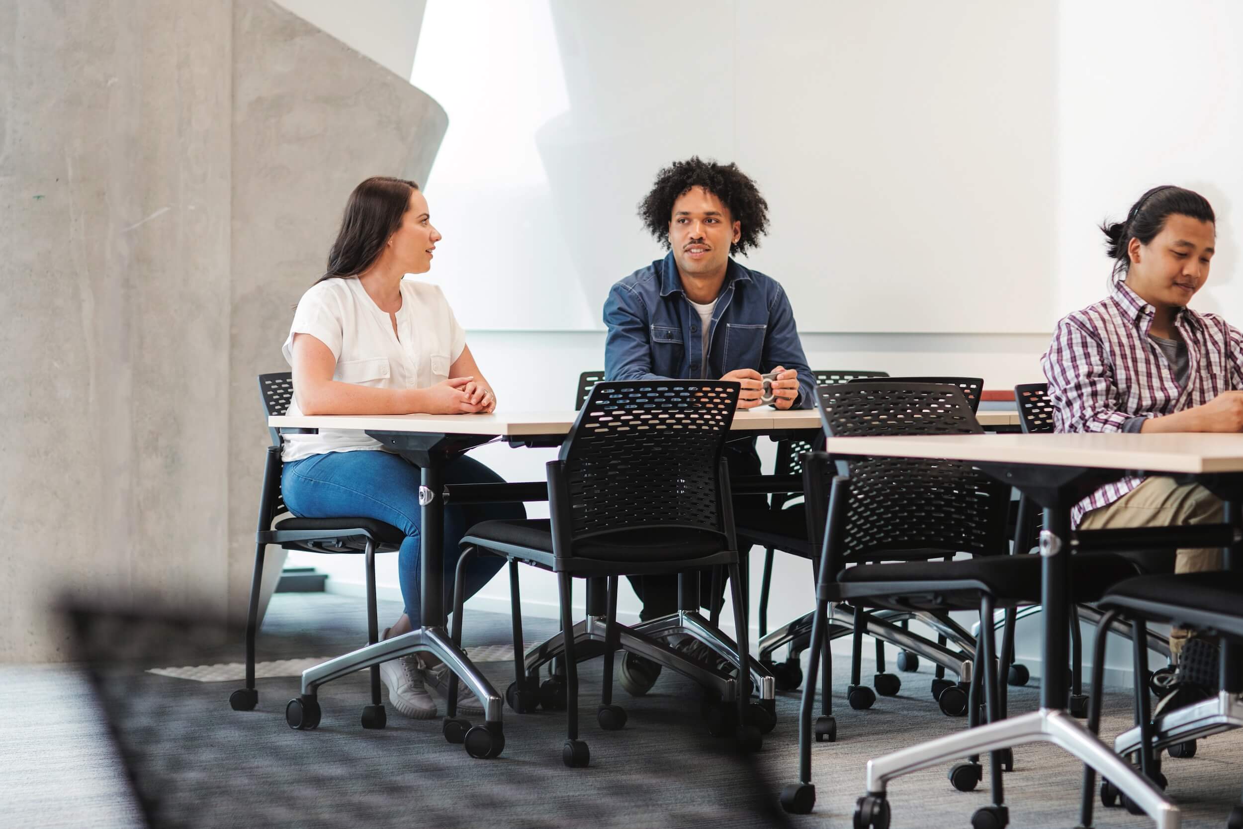 Group of three people sitting at tables in a workshop setting