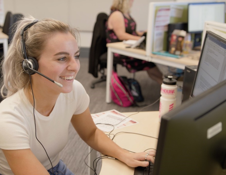 Female student support staff wearing a headset and using a computer to answer student enquiries.