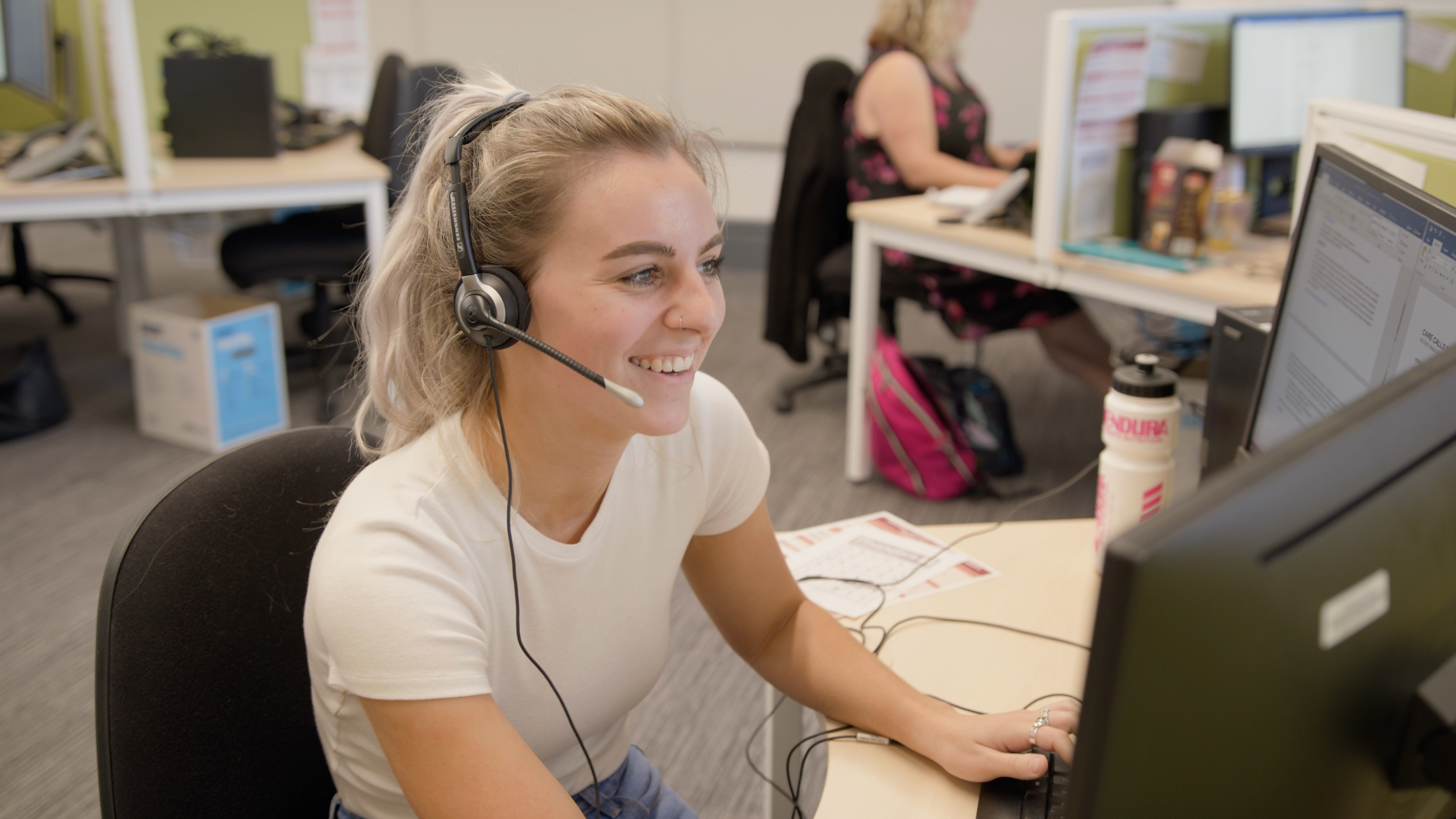 Female student support staff wearing a headset and using a computer to answer student enquiries.