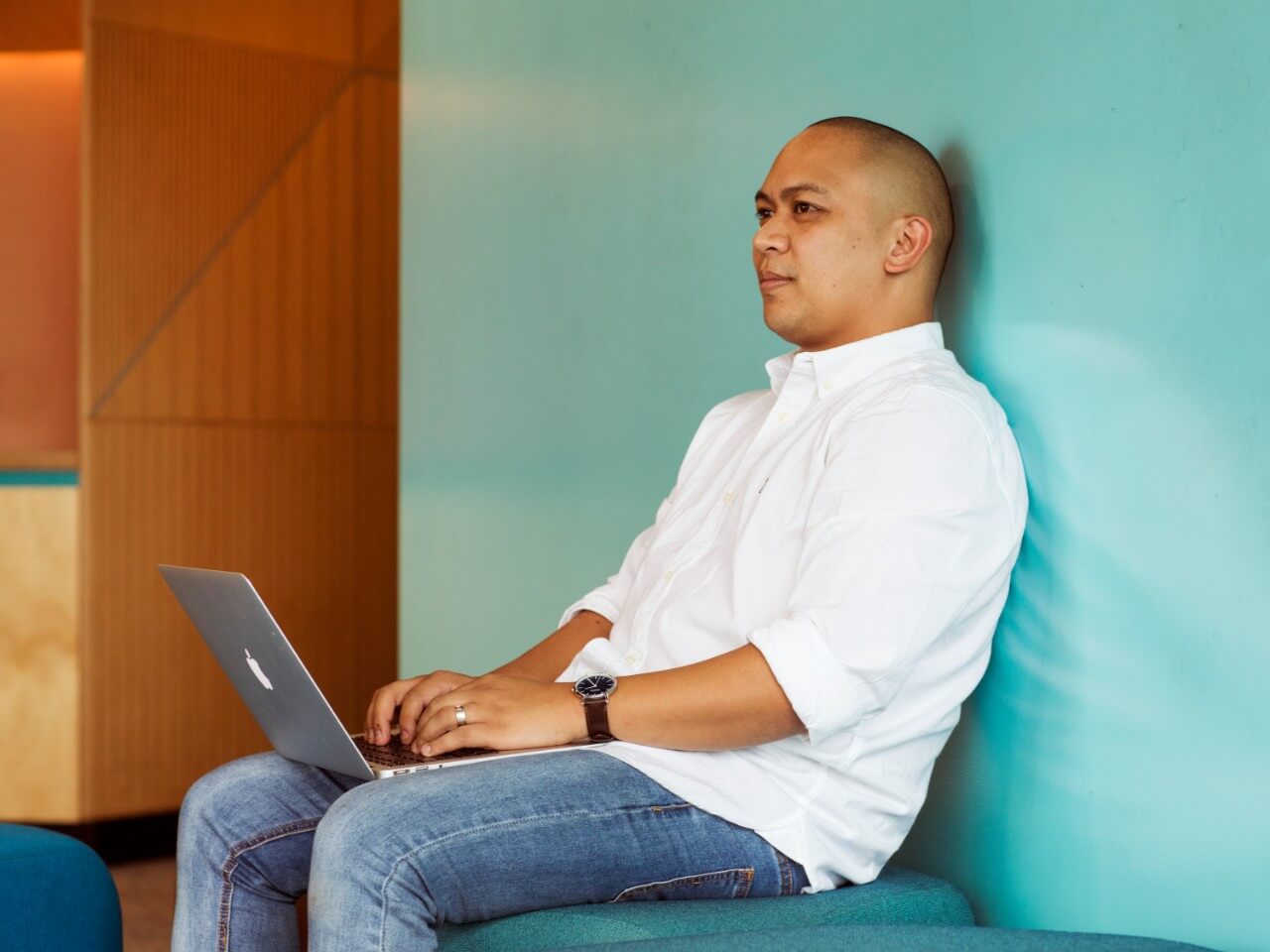 Postgraduate student sitting with a laptop against a wall with a teal background