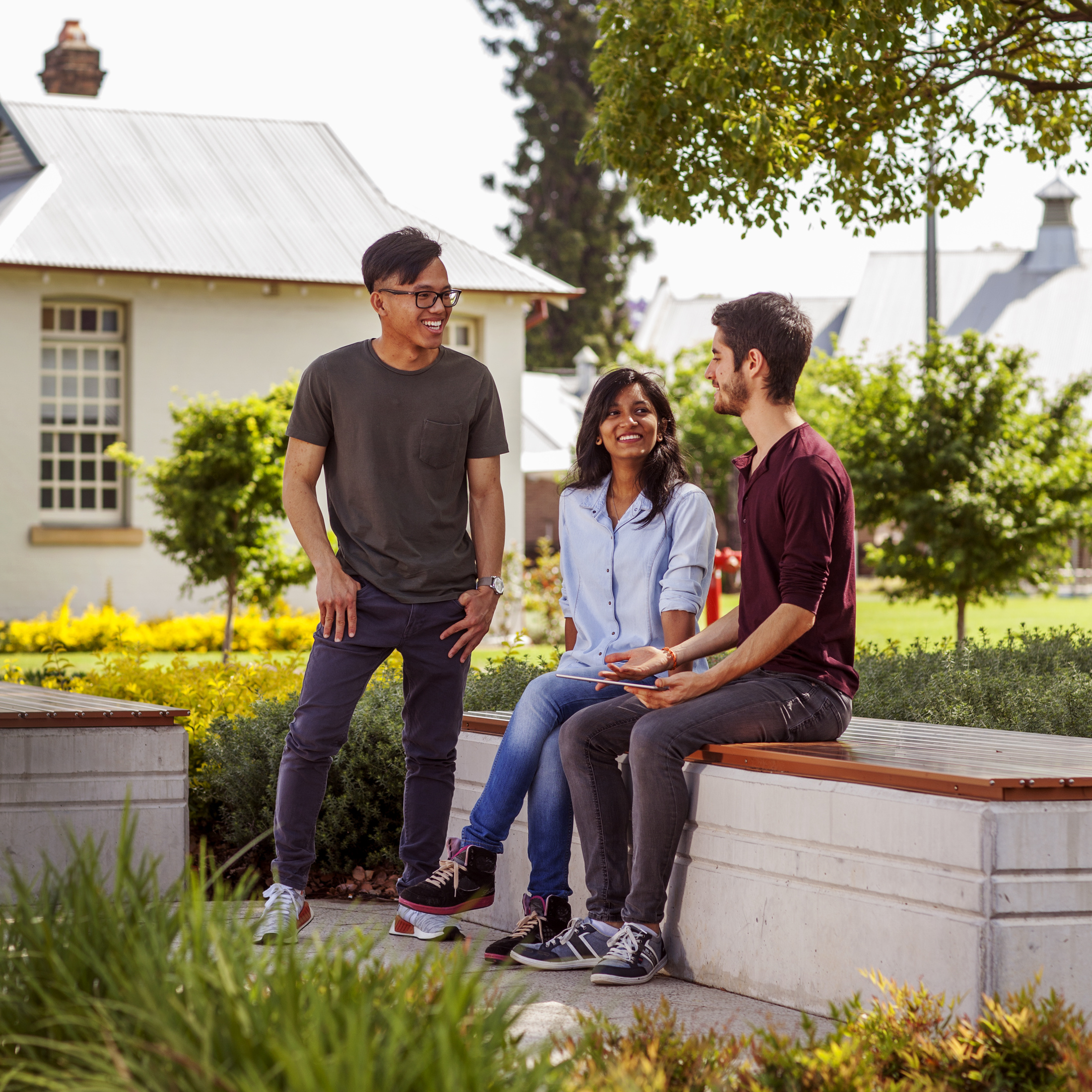 A group of three students standing and sitting outside