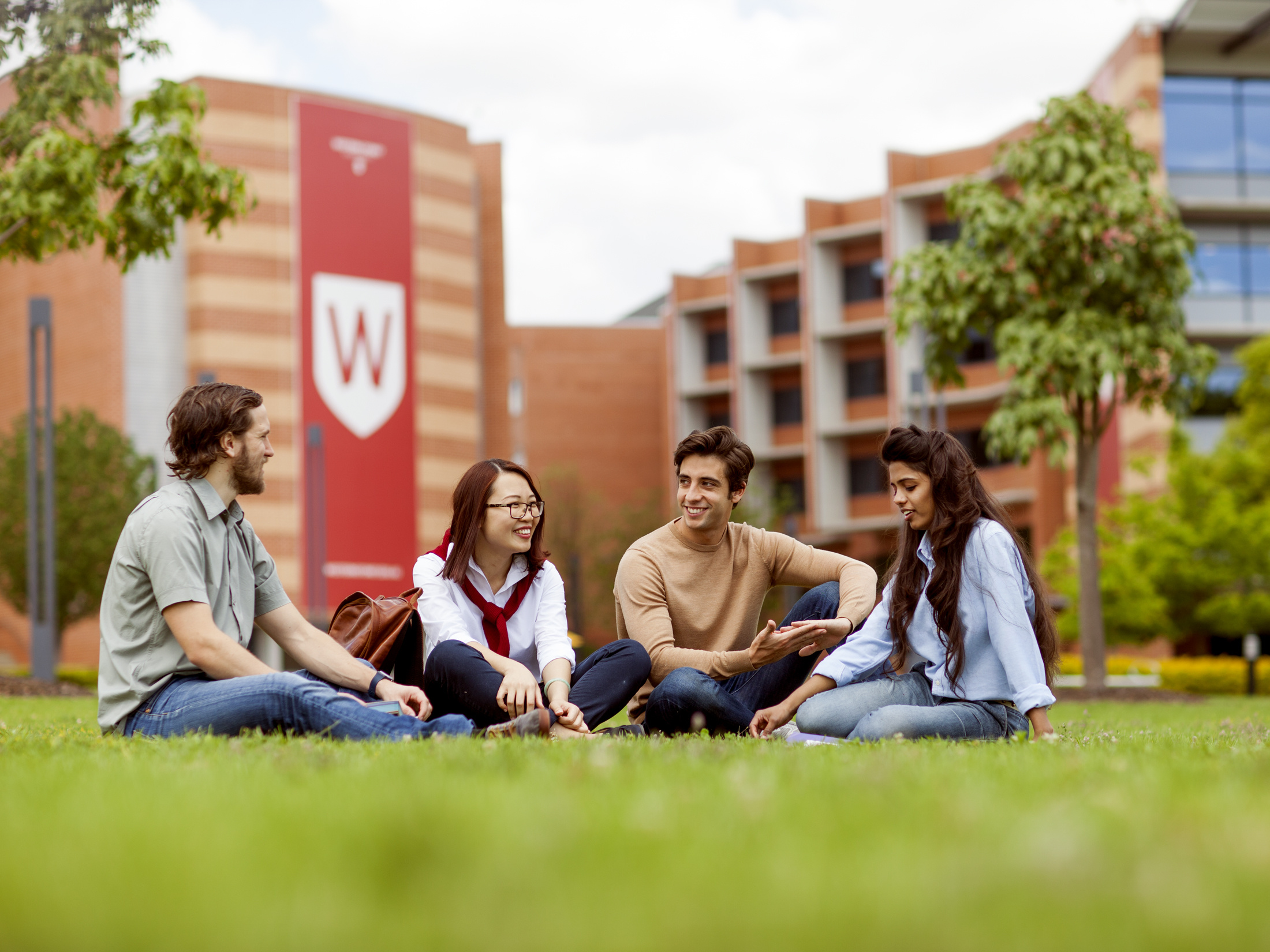 A group of four students sitting on the grass outside Western Sydney University's EA building at Parramatta South campus