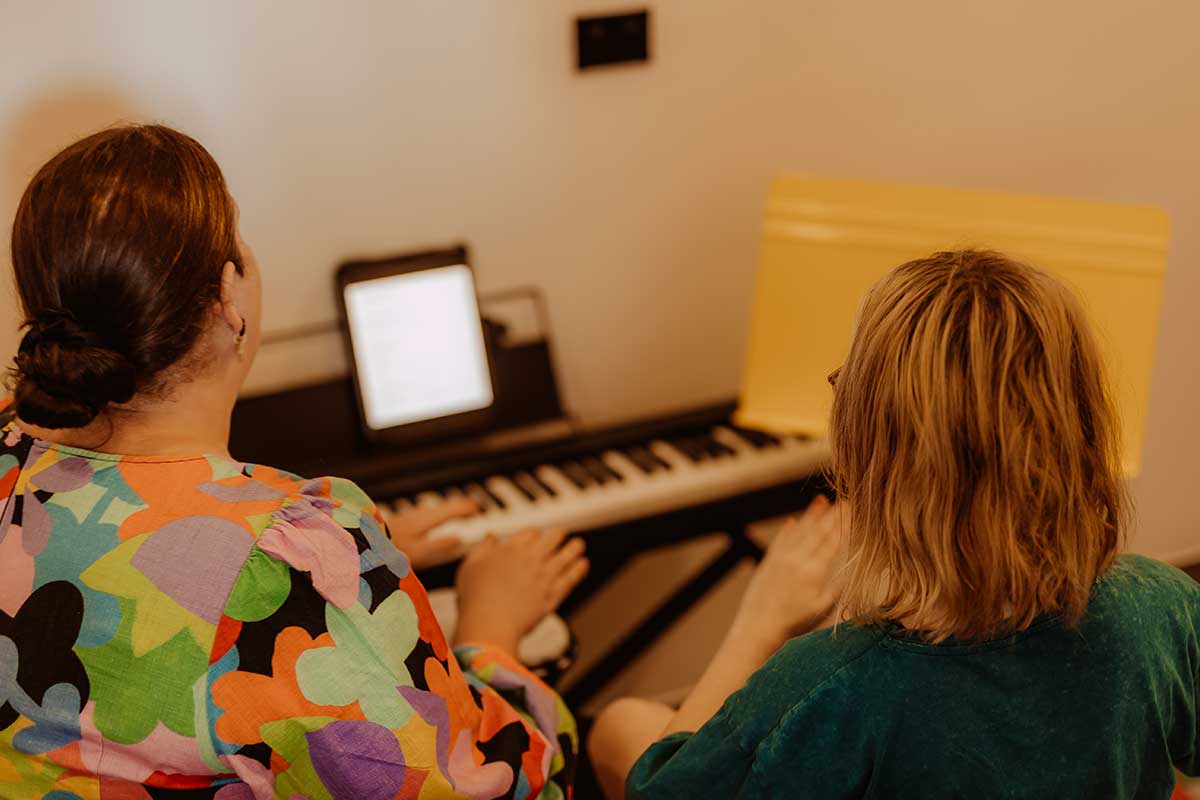 two females with back facing the camera sitting in front of keyboard with ipad screen on top