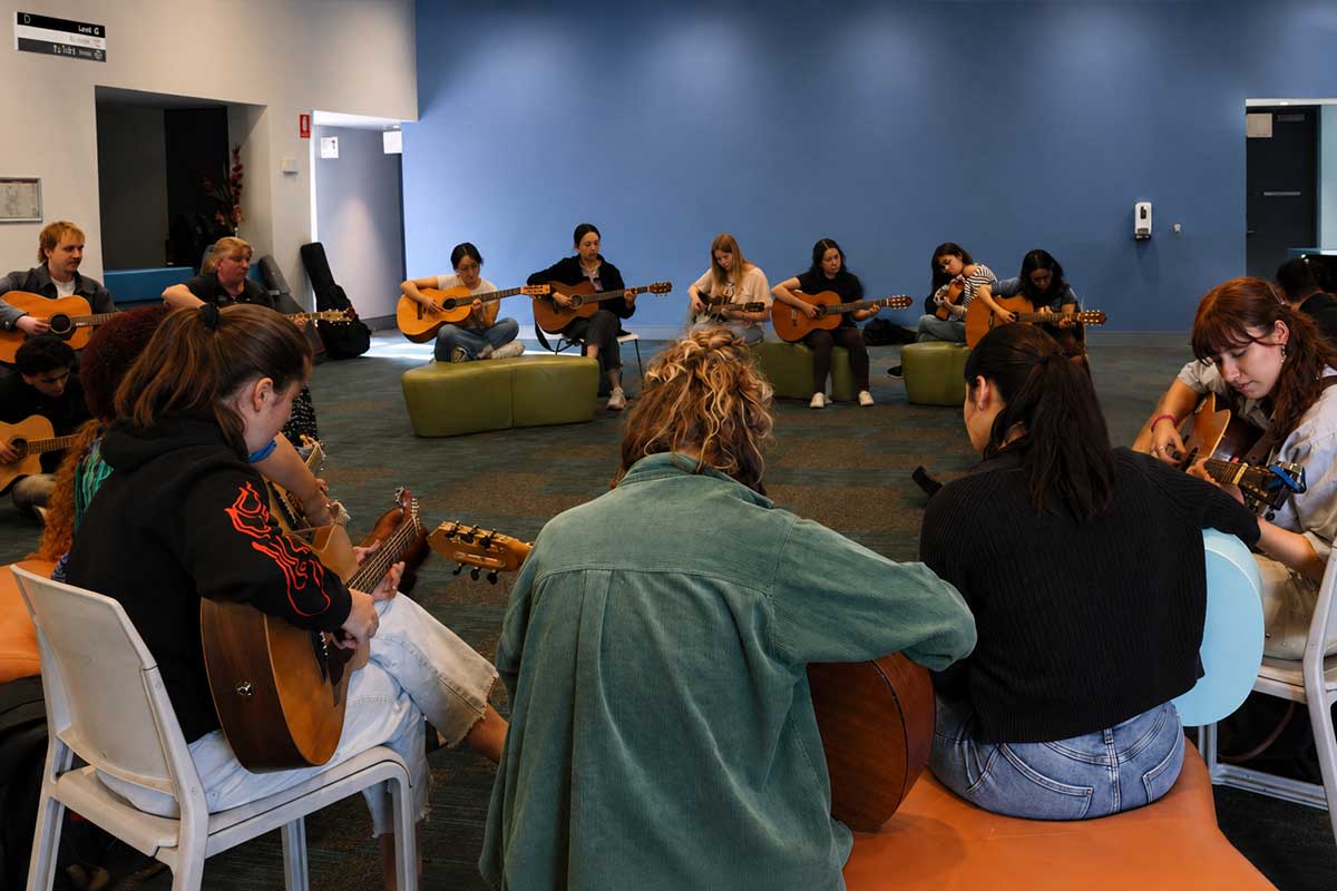 students sitting on chairs in a circle playing guitars