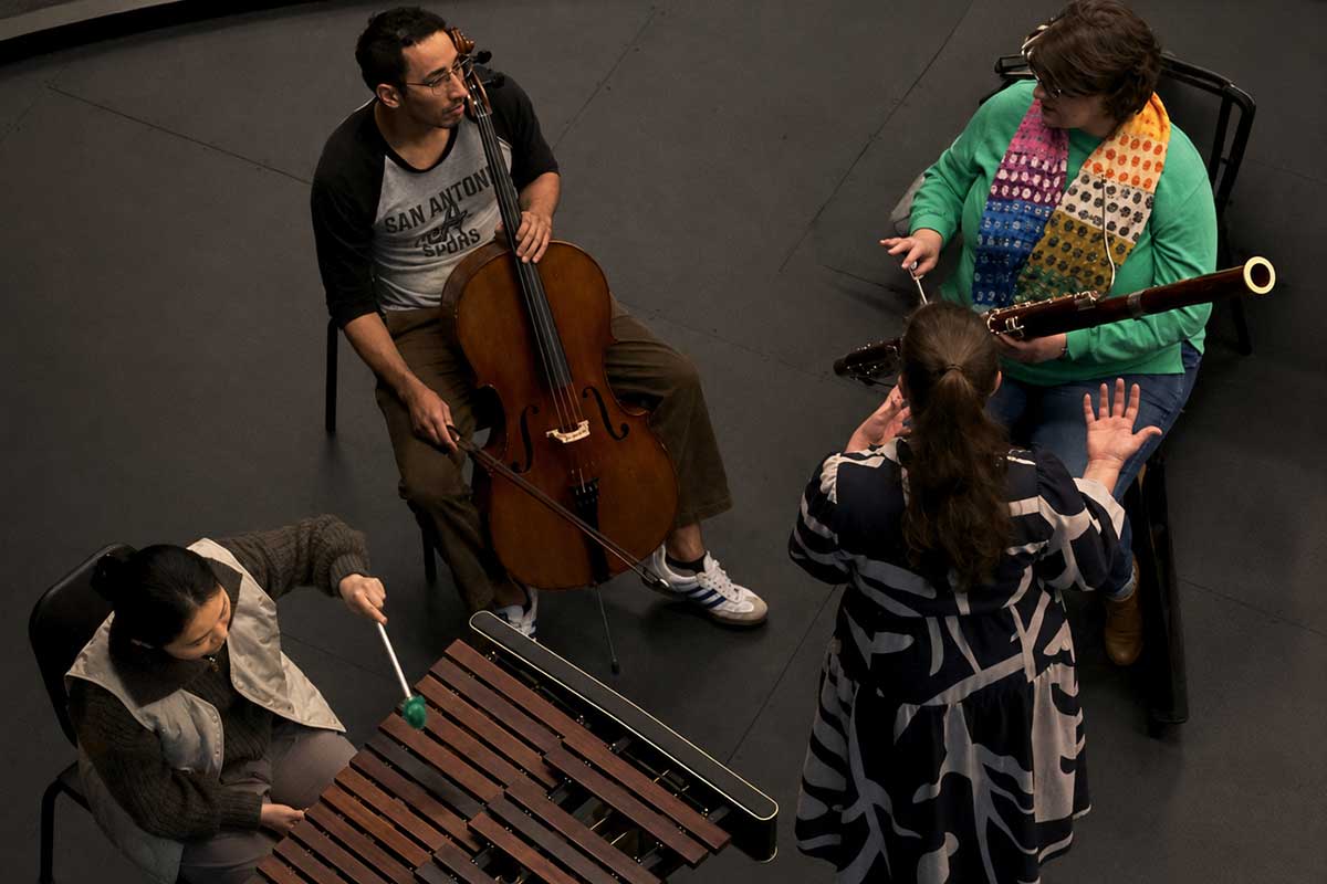 aerial view of 4 students sitting a circle on chairs with music instruments