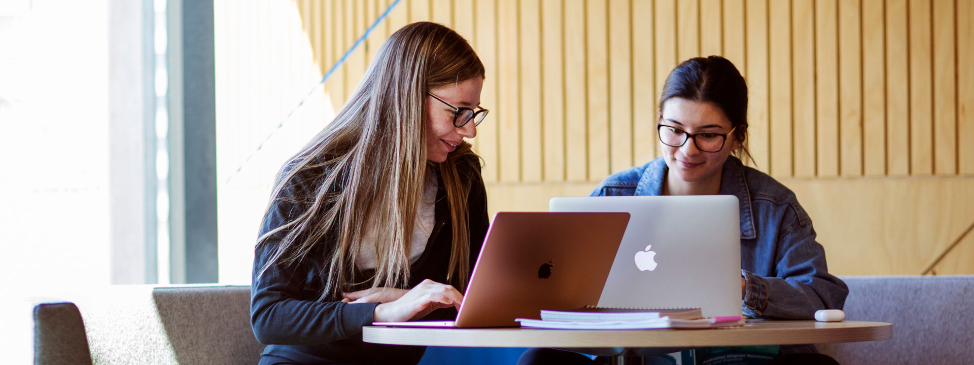 Two female students studying at a table with laptops.