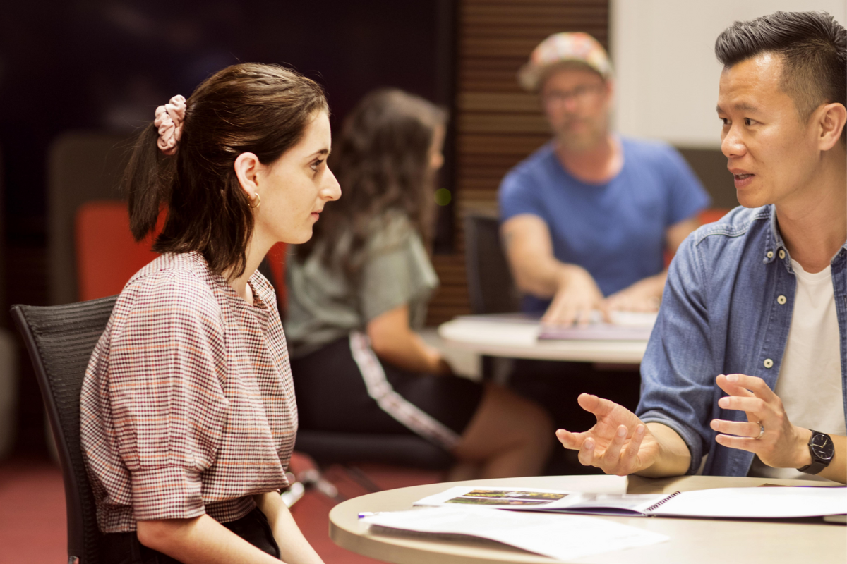 A female student is sitting at a table talking to an older man
