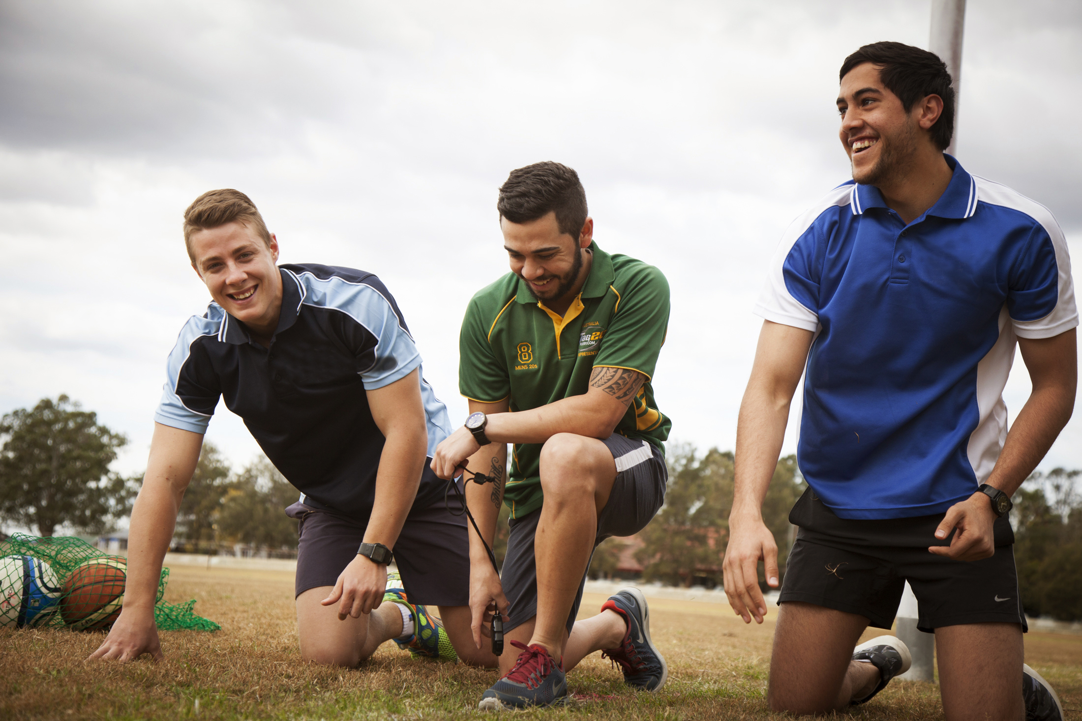 Three male students kneeling in a sports field and laughing