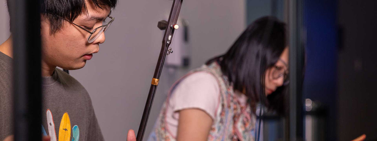 two students sitting in studio playing string instrument and a xlylophone