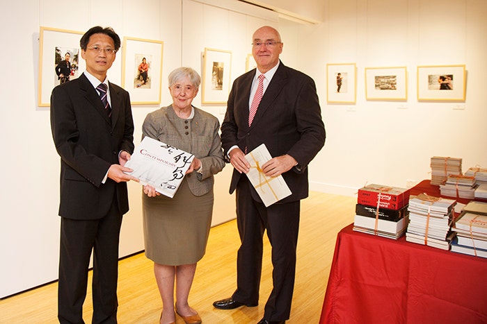 Barney Glover, Jocelyn Chey and visitor stand inside the Institute holding donated books. Books are sitting on a table beside them and artwork hangs on the walls.