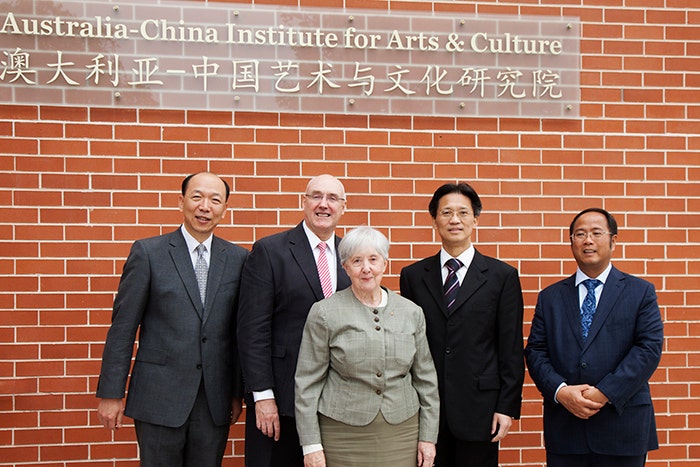 Barney Glover, Jocelyn Chey and three visitors stand in front of the Australia-China Institute for Arts and Culture sign and brick wall.