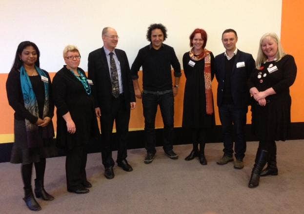 Professor Arvanitakis in a room with 6 other people from RMIT University, orange background
