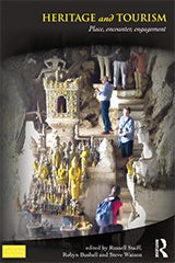 The cover of the book Heritage and Tourism which shows tourists at an Asian site where there are statues carved into the rock.