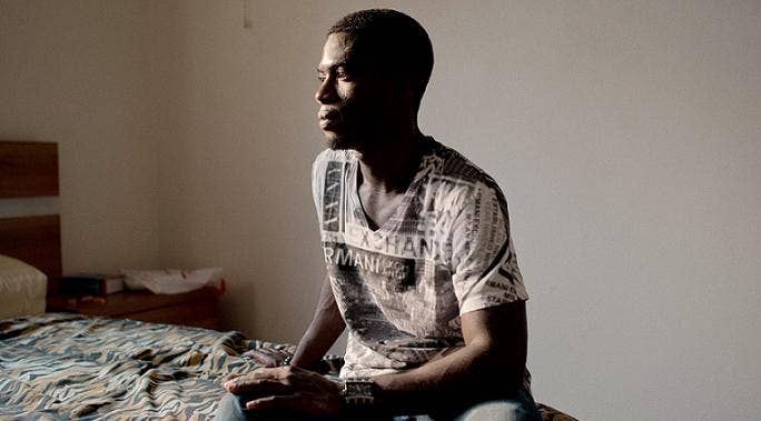 Young man sitting on a bed looking pensive, and away from the camera