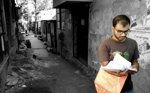 A man stands in a narrow alleyway looking at a stack of papers in his hand. He is pictured in colour. The alleyway is in black and white.