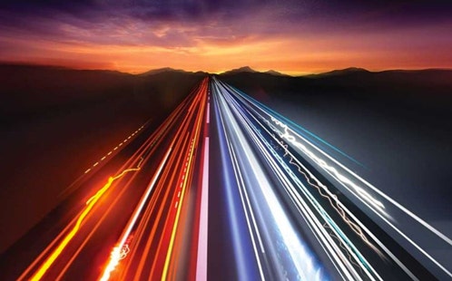 Photo of a highway of lights leading towards a sunset.