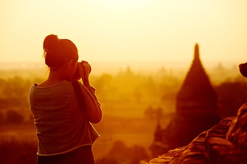A young woman photographing a view in the sunset.
