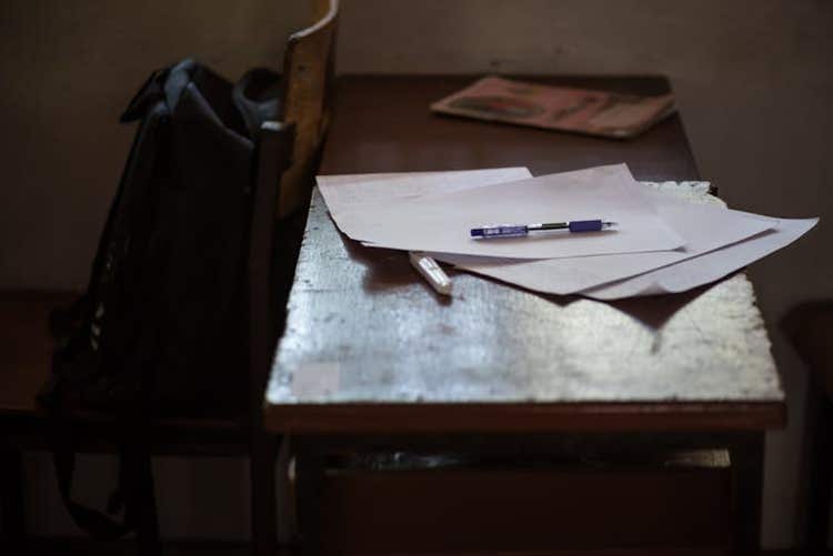 Sheaf of papers and pens on a desk in a dark room.