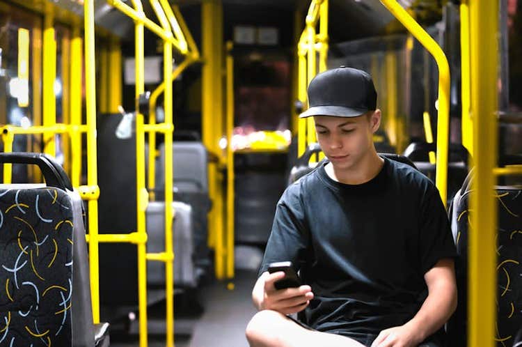 Teenage boy wearing cap on bus looking down at smartphone