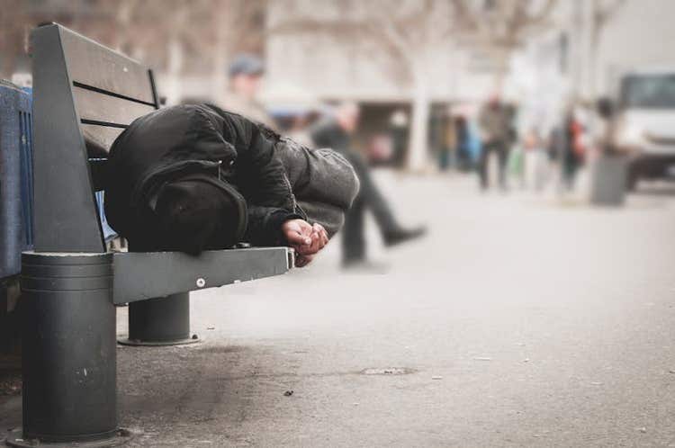 Homeless man sitting on a public bench, hunched over.