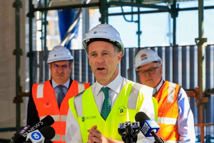 Man in high-vis vest and hard hat speaks into media microphones