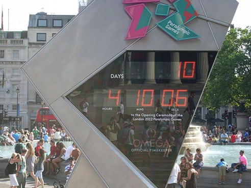 A screen in Trafalgar Square counts down to the Paralympic Games: 10 days, 4 hours, 10 minutes, 6 seconds. People sit by the fountain behind it.
