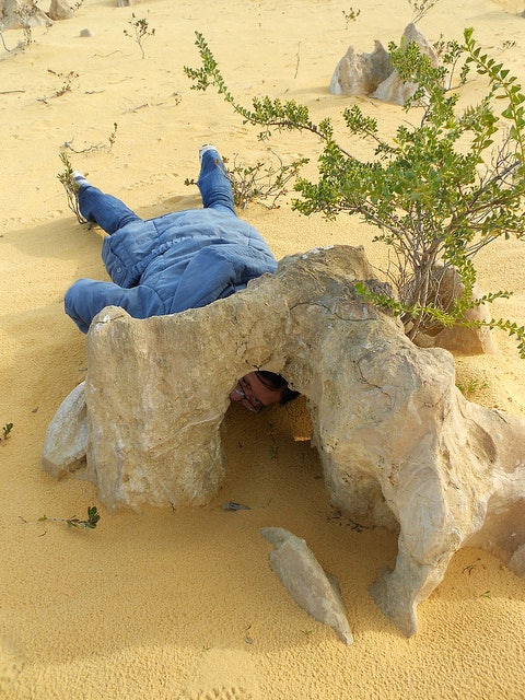Jen Li laying on the desert inspecting a big rock