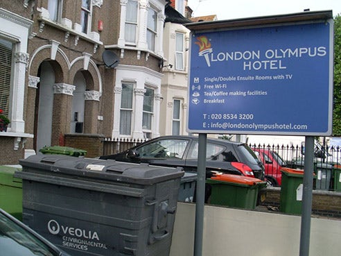A sign outside a hotel reads 'London Olympus hotel'. There are overflowing rubbish bins on the street directly outside.