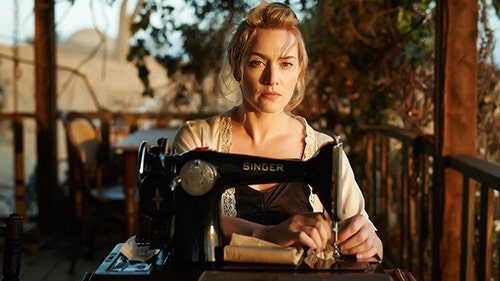 Scene from the movie The Dressmaker - Kate Winslet sits at a Singer sewing machine on a wooden veranda.