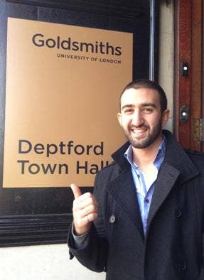 Kev Dertadian stands in front of a Goldsmiths University sign
