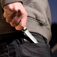A close-up photo of a young man's hand pulling a knife out of his pocket.