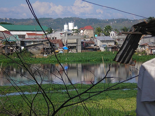 Poor quality houses next to a flooded field with hills in the distance.