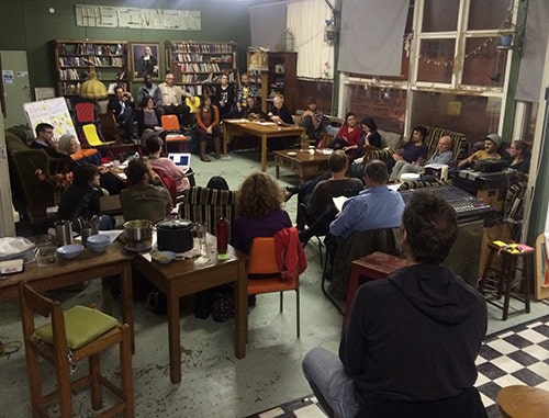 Group of approximately 30 people sitting on couches and chairs, in discussion.