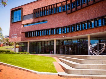 Red brick library building with large glass windows, green lawn and curved concrete steps in the foreground.